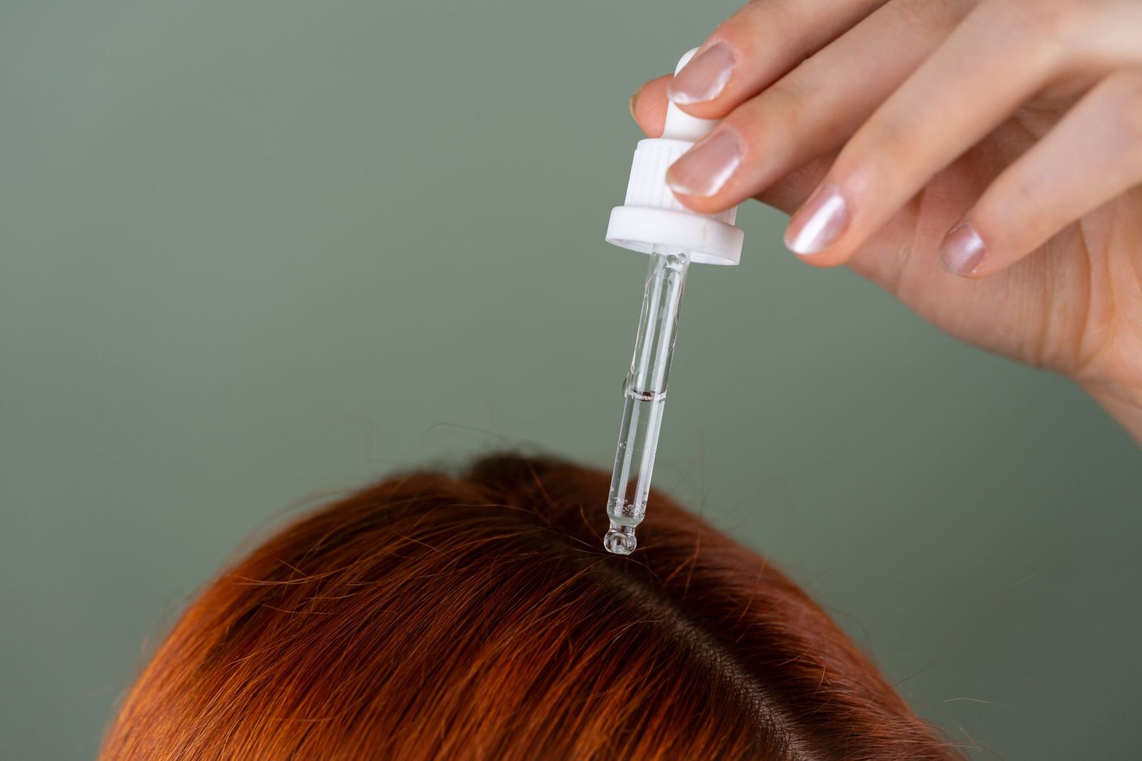 Manos aplicando aceite vegetal con las yemas sobre la raíz del cabello